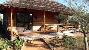 Una cabaña rústica de madera con techo de paja, un área de estar al aire libre y un sendero de tierra que conduce a la entrada.
