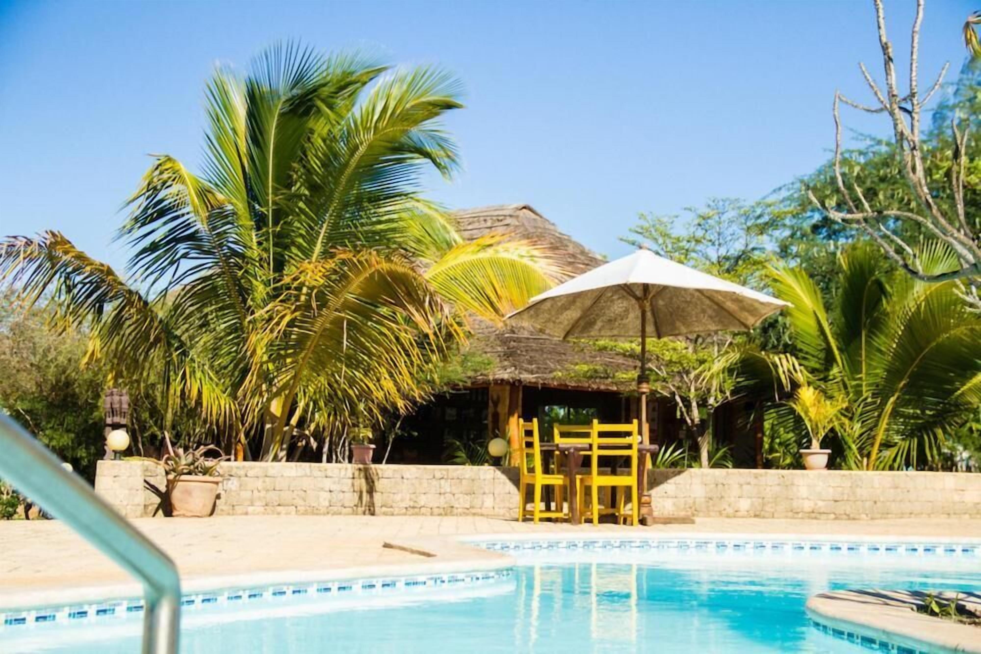 Un área de piscina con una cabaña techada de paja, palmeras y un cielo azul despejado.