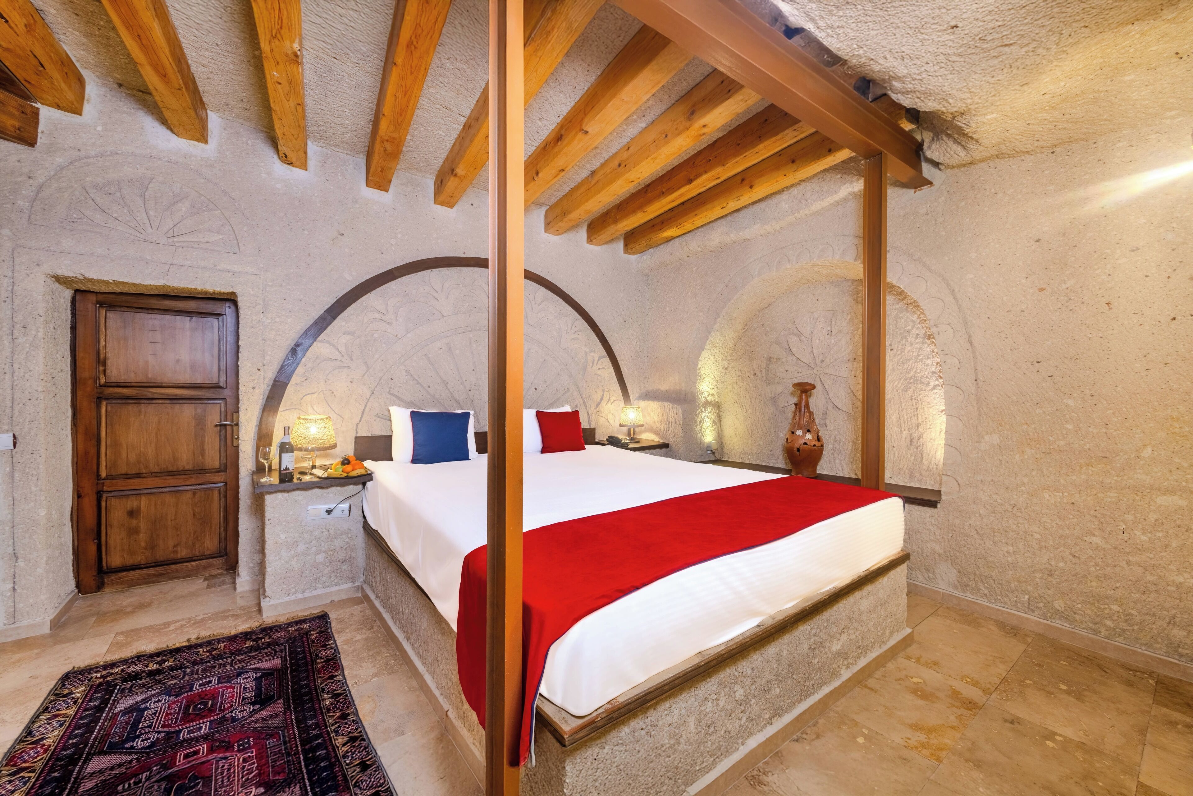 A bedroom with a four-poster bed, a wooden wardrobe, and a nightstand with a lamp.