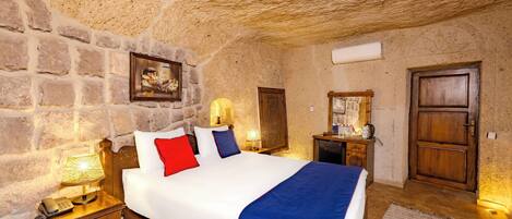 A bedroom with a stone wall, a wooden bed, a nightstand with a lamp, and a wooden wardrobe.
