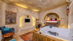 A room with a large bathtub, a wooden bar, a sofa, and a painting on the wall. - Grand Elite Cave Suites (Nevsehir)