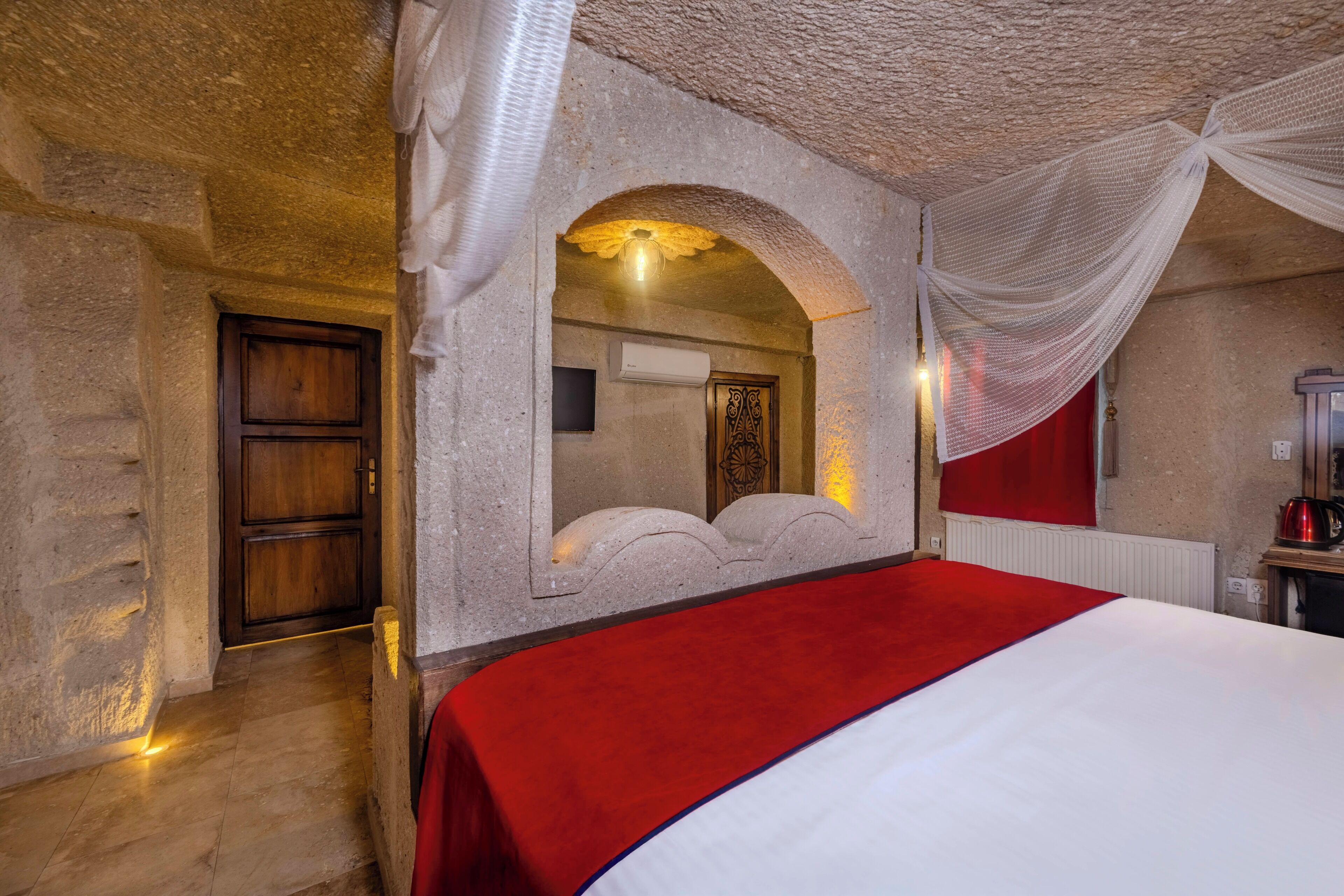 A bedroom with a large bed, a wooden door, a mirror, and a red curtain.