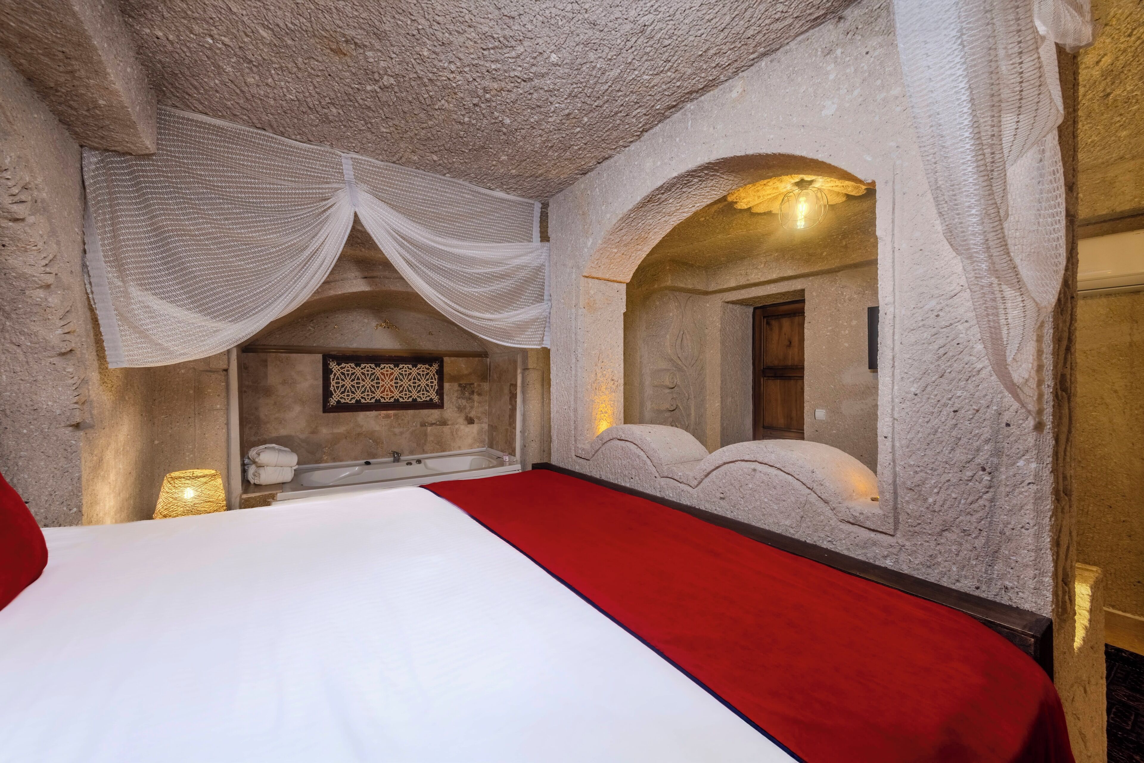 Un dormitorio con una cama grande, un corredor rojo y una pared de piedra con una ventana.