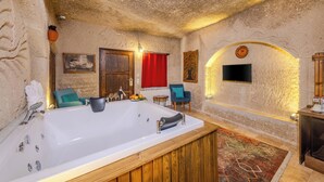 A spa room with a large bathtub, wooden paneling, a red curtain, a blue chair, and a television mounted on the wall. - Grand Elite Cave Suites (Nevsehir)