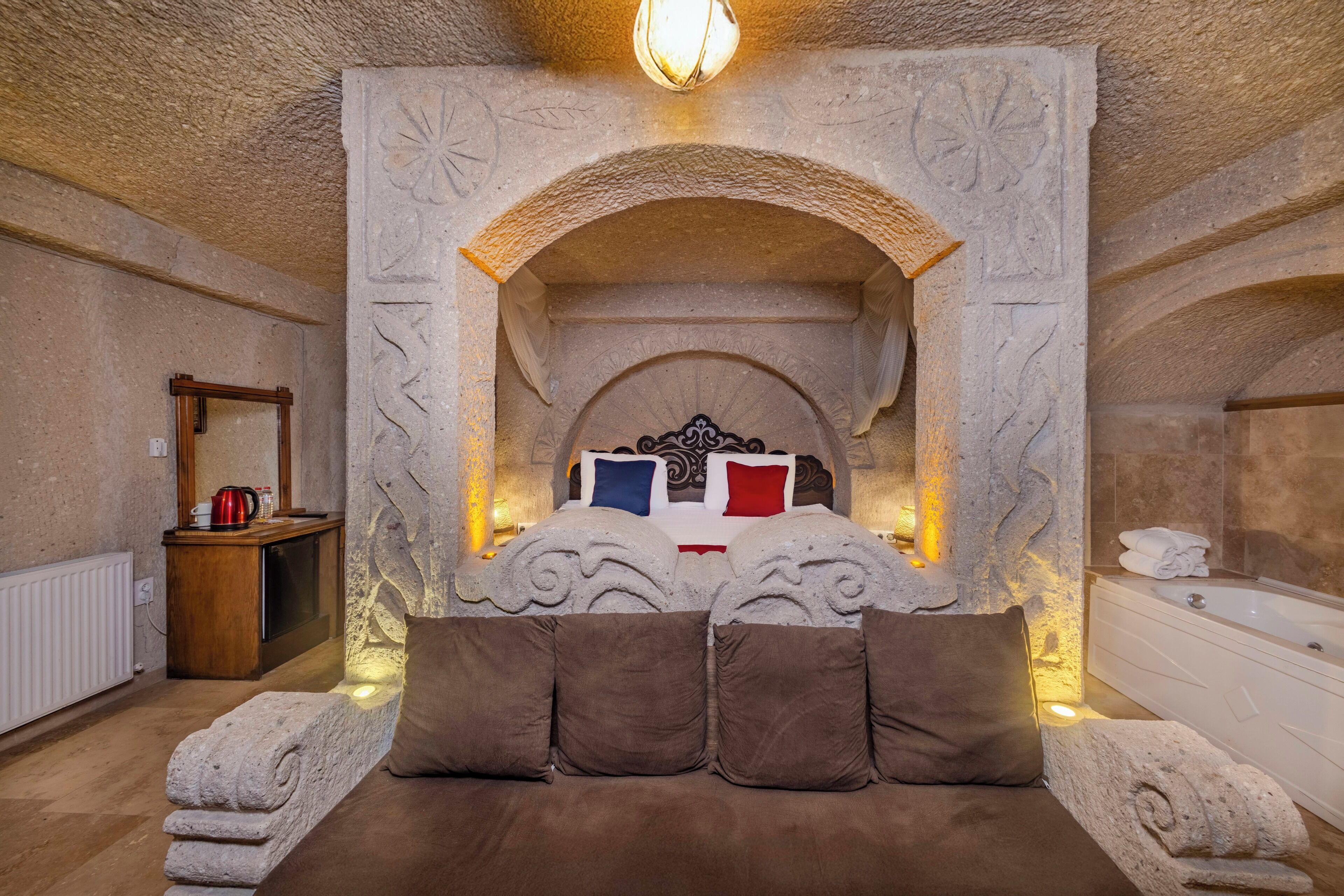 Una camera da letto con un camino in pietra, un letto con cuscini, un comodino in legno e una vasca da bagno.