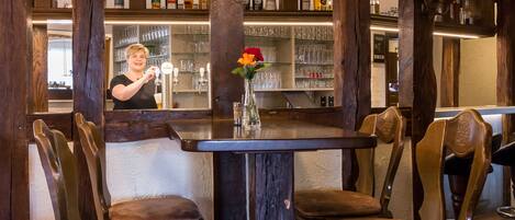 A bar area with wooden chairs, a bar counter, and shelves stocked with bottles and glasses.