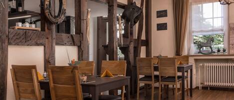 A dining area with wooden chairs and tables, a horse sculpture, and a window with curtains.