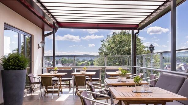 Un espace extérieur aménagé en terrasse, avec plusieurs tables et chaises, des plantes en pot et une vue sur le paysage.