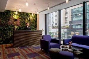 Un área de recepción moderna con una pared verde, un mostrador de madera y asientos con vistas a la ciudad.