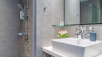 Uma casa de banho moderna com chuveiro, lavatório branco e prateleira de vidro.