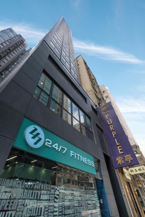 Un edificio moderno con gimnasio abierto las 24 horas, grandes ventanales y un llamativo letrero morado.