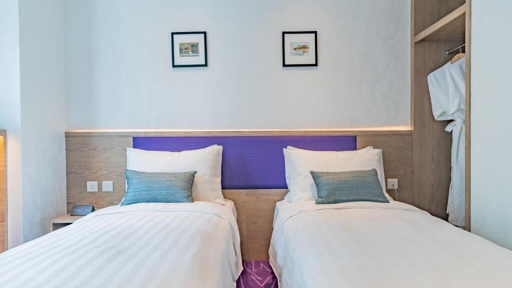A hotel room with two beds, a wooden headboard, a nightstand, and a wardrobe.