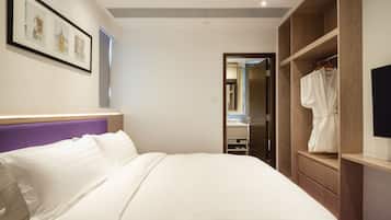 Une chambre d’hôtel avec un grand lit, une armoire en bois, une salle de bain avec un miroir et un tableau encadré au mur.