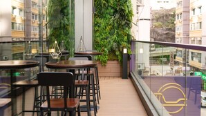 Een modern buitenverblijf met tafels, stoelen, een glazen hekwerk en een verticale tuinmuur.