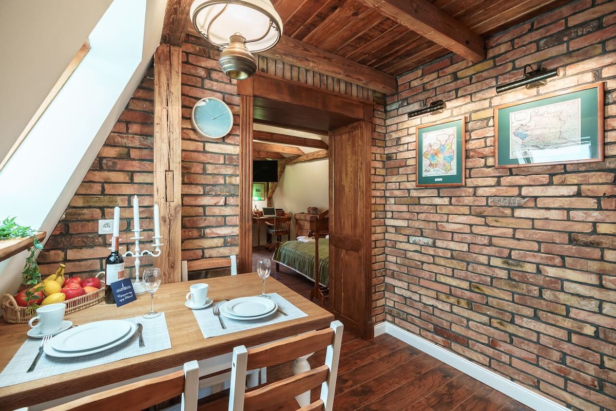A dining area with a brick wall, wooden ceiling beams, and a table set for two.