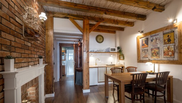 A rustic kitchen with a wooden table and chairs, a brick wall, and a clock on the wall. - Old House Apartments Poznań (Poznan)