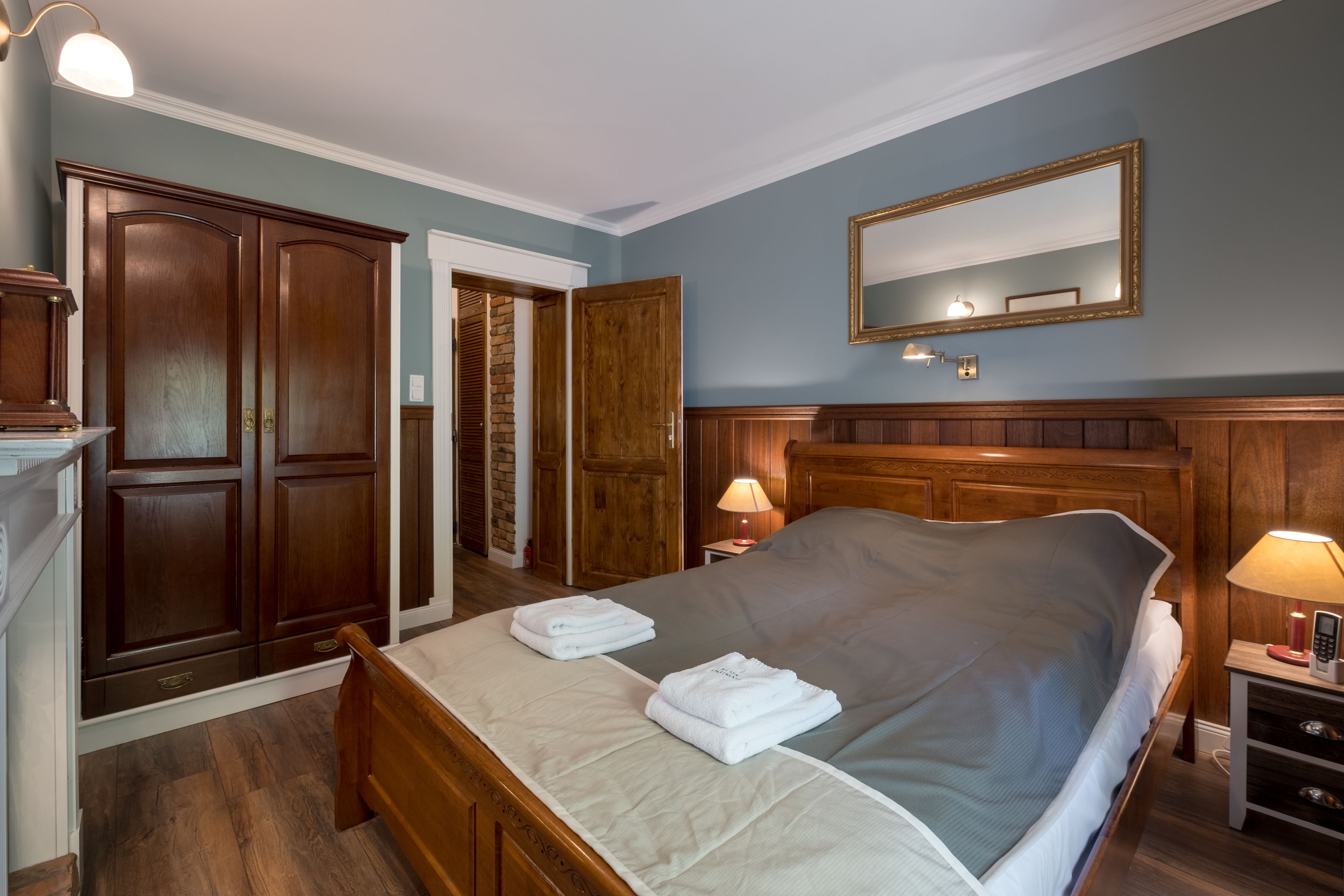 Een slaapkamer met een groot bed, een houten garderobe en een spiegel aan de muur.