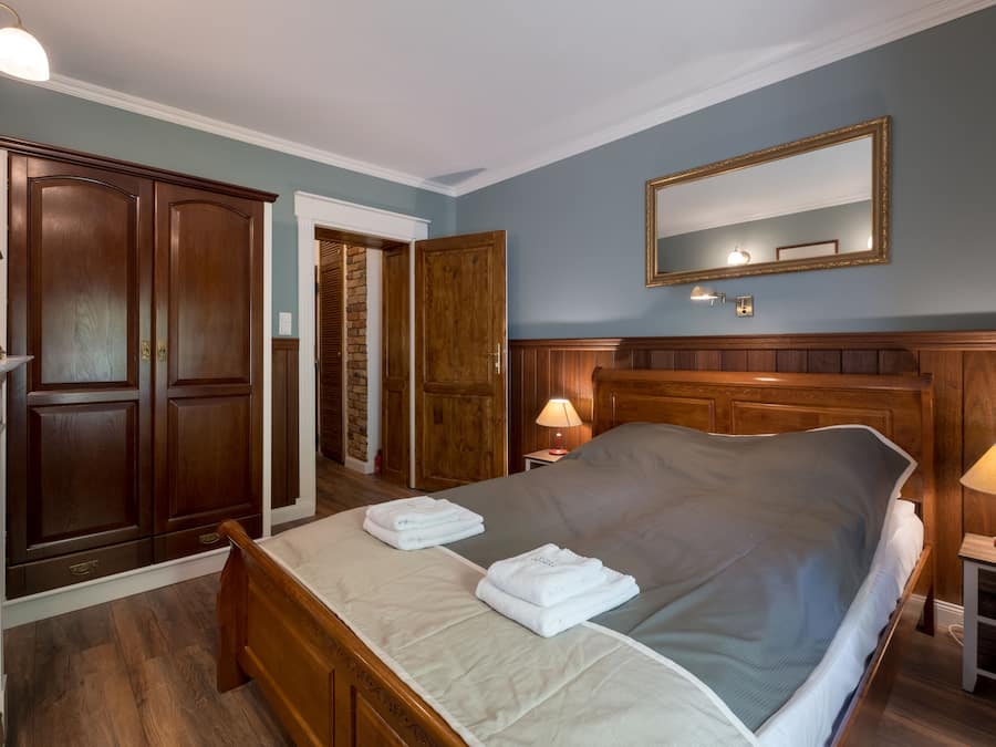 Een slaapkamer met een groot bed, een houten garderobe en een spiegel aan de muur.