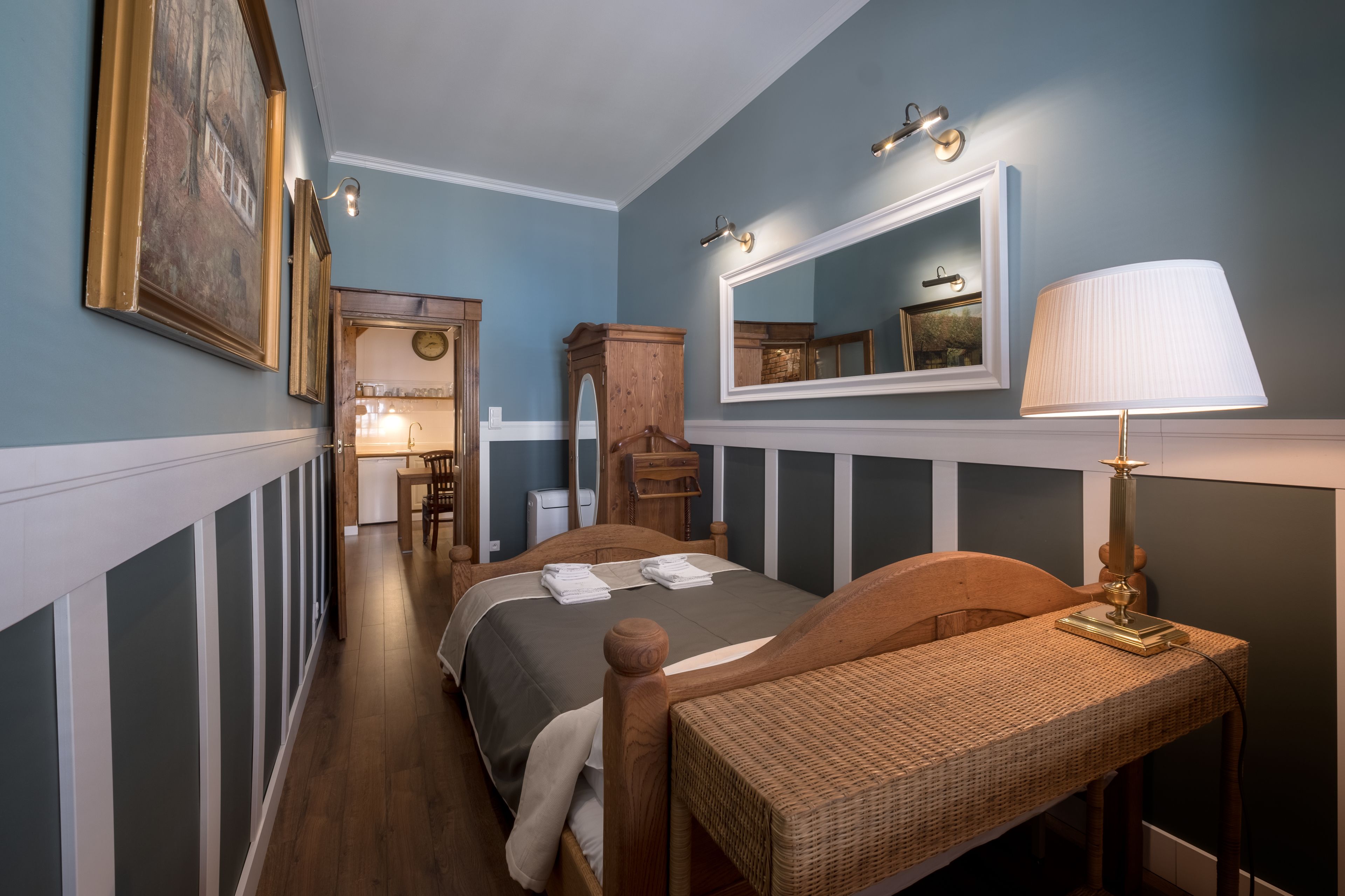 A bedroom with a bed, a bedside table with a lamp, a wooden chair, a dresser, and a mirror.