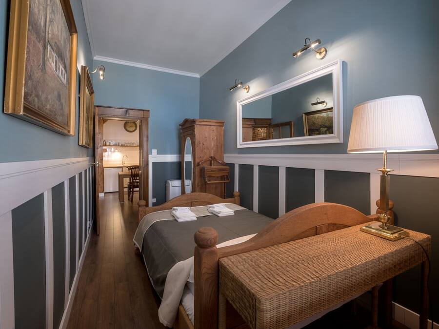 A bedroom with a bed, a bedside table with a lamp, a wooden chair, a dresser, and a mirror.