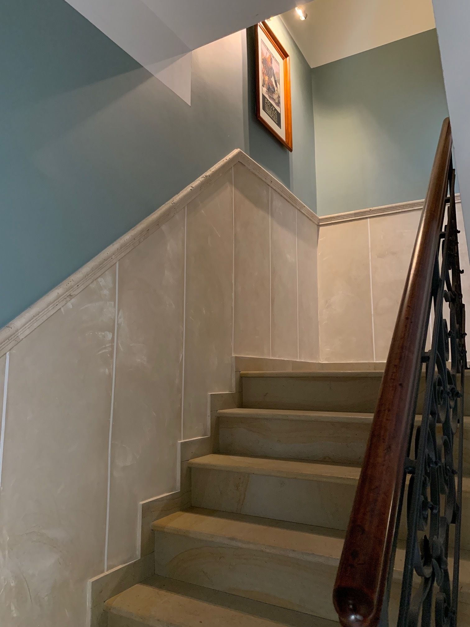 A staircase with a wooden handrail and white wall paneling.