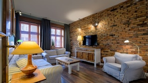 A living room with striped sofas, a wooden coffee table, a TV on a brick wall, and a lamp on a side table. - Old House Apartments Poznań (Poznan)