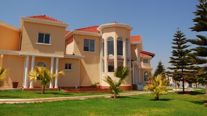 Un edificio de varios pisos con techo de tejas rojas, amplias ventanas y un césped bien cuidado con palmeras.