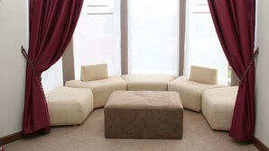 Salón de esquina con un sofá seccional color beige, un reposapiés a juego y cortinas color ciruela.