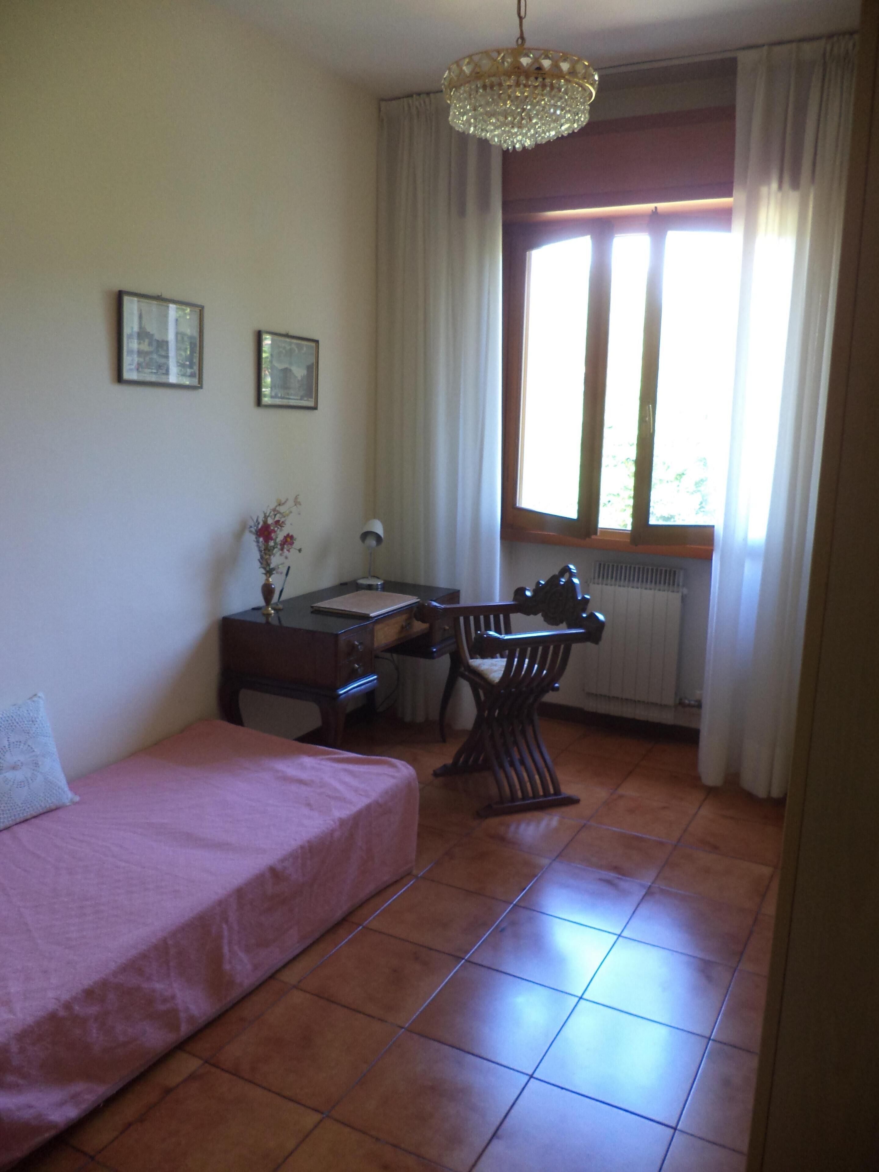 Een kamer met een bed, een bureau, een stoel en een raam met gordijnen.