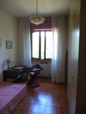 Une pièce comprenant un lit, un bureau, une chaise, un radiateur et une fenêtre avec des rideaux.