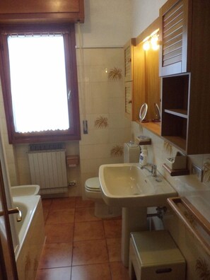 Une petite salle de bain comprenant des toilettes, un lavabo et une fenêtre avec des stores.