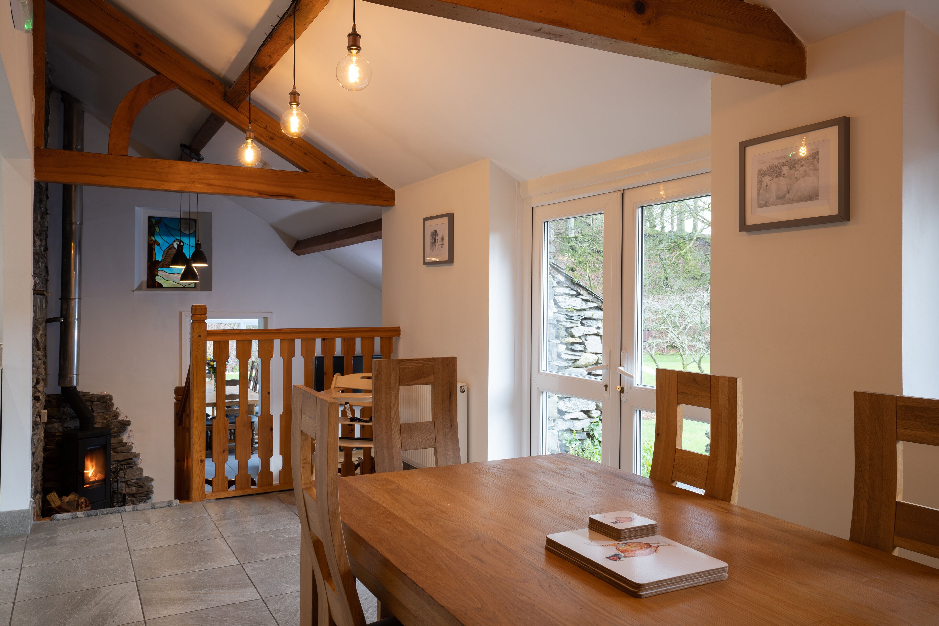 A dining area with a wooden table, chairs, a fireplace, and a view of the outdoors through a glass door.