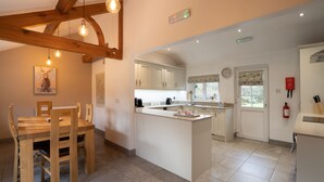 A modern kitchen with wooden beams, a dining area with a table and chairs, and a small island with a sink. - Low Jock Scar Country Estate (Kendal)