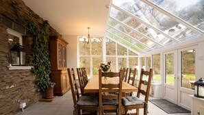 A dining area with a wooden table and chairs, a chandelier, and a view through a glass enclosure. - Low Jock Scar Country Estate (Kendal)