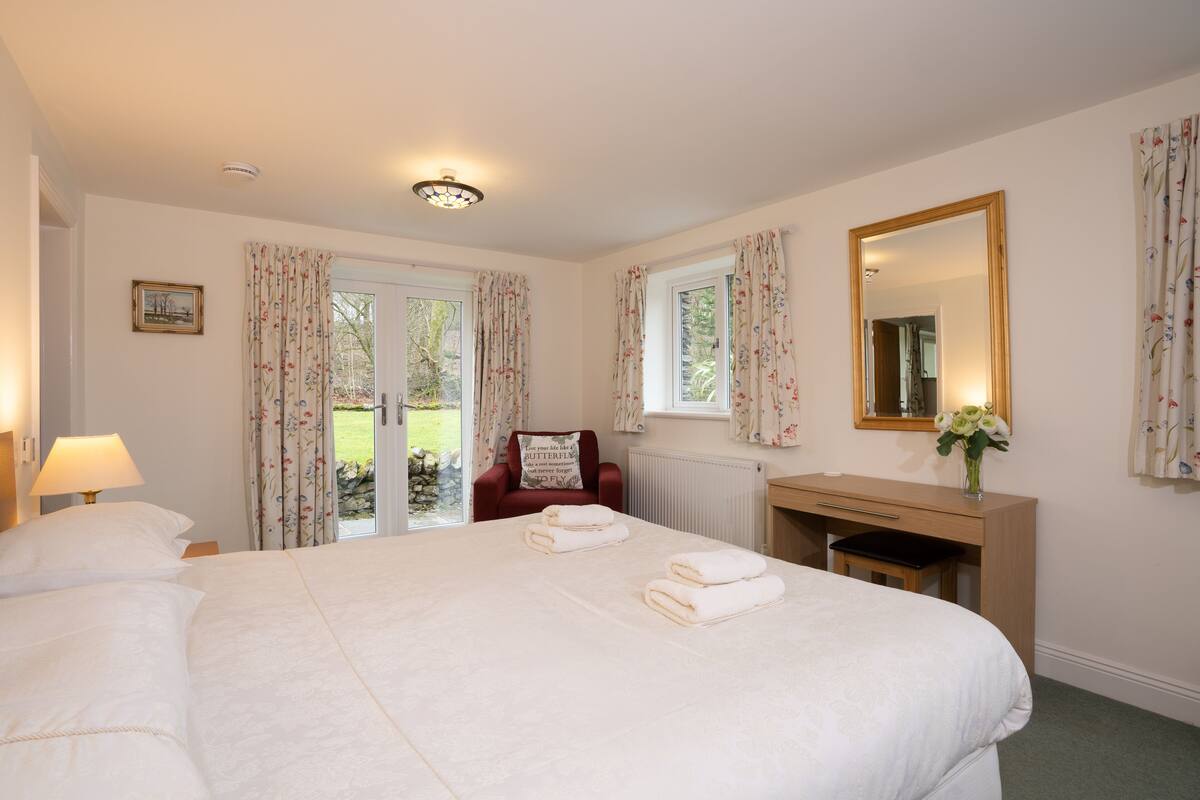 A hotel room with a large bed, a desk, a chair, a mirror, and a view of the outdoors.