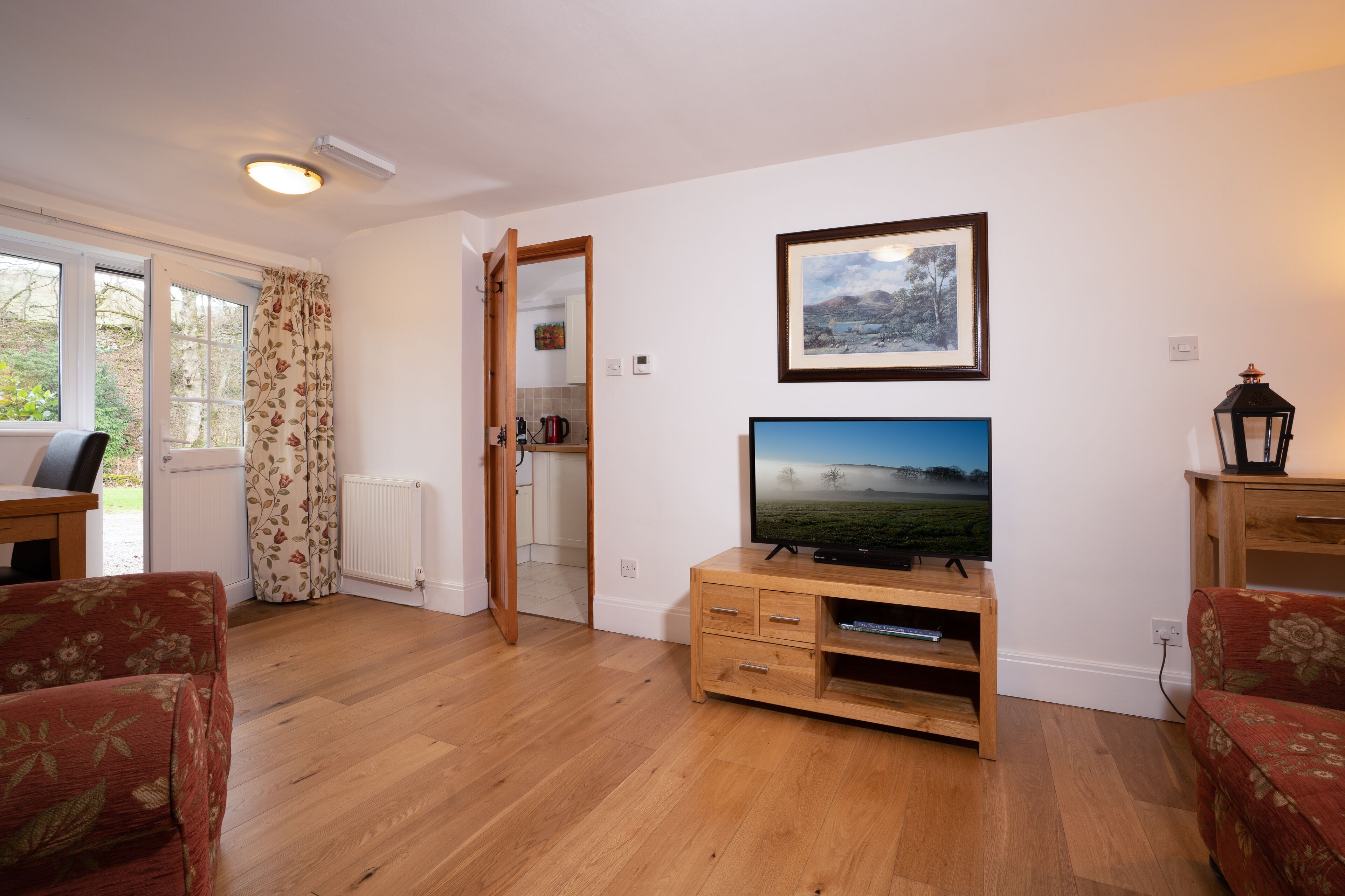 Een woonkamer met een houten tv-meubel, een lijst met een foto aan de muur en een uitzicht door een open deur.