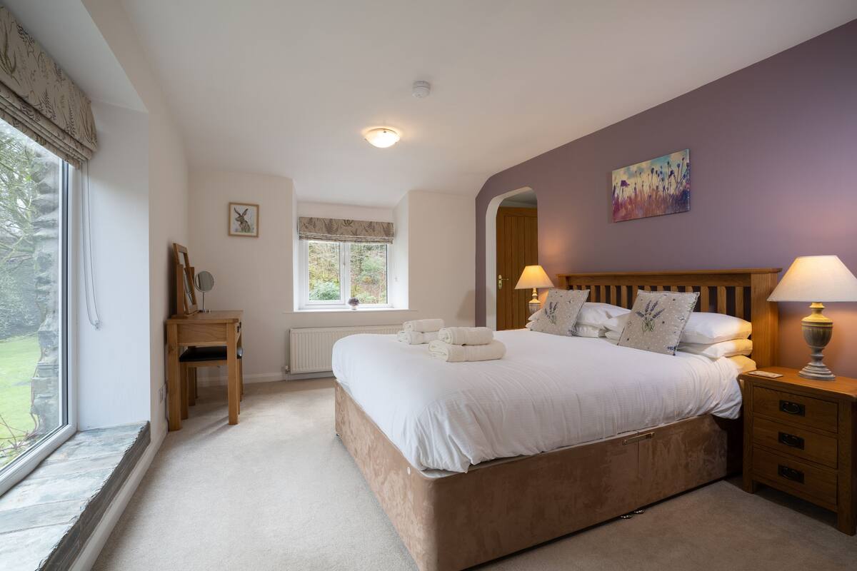 A bedroom with a large bed, bedside lamps, a wooden nightstand, a window with a view, and a radiator.
