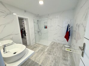 A modern bathroom with a white sink, a glass-enclosed shower, and marble walls.