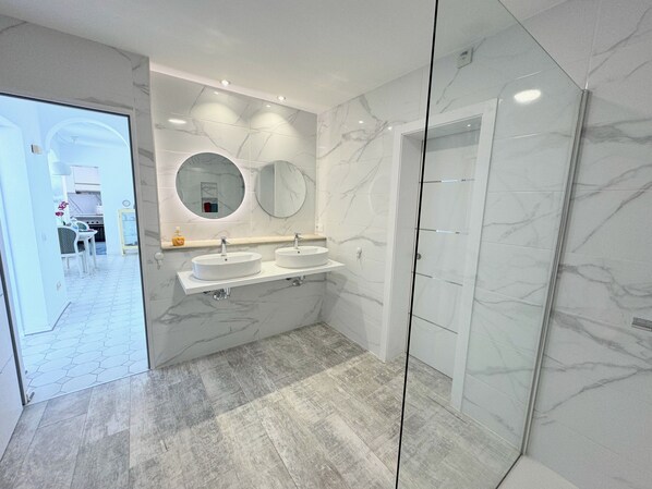 Un baño moderno con dos lavamanos, un espejo grande y una cabina de ducha de vidrio.
