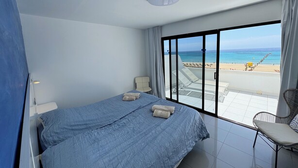 Habitación de hotel con una cama grande, una silla y vista a la playa.