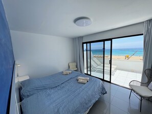 Habitación de hotel con una cama grande, una silla y vista a la playa.
