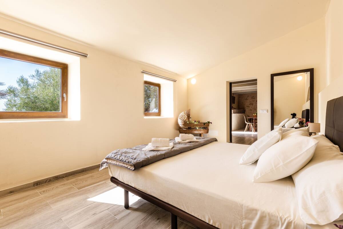A bedroom with a large bed, a window, a mirror, and a view of the outdoors.