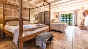 Una cama con dosel, un banco, una mesita de noche y una ventana con cortinas.