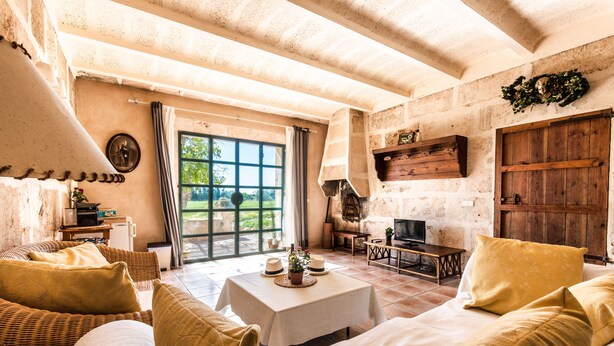 Una habitación acogedora con una cama grande, una mesa con un adorno decorativo, muebles de mimbre y una pared de piedra.