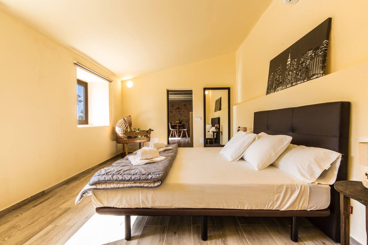 A bedroom with a large bed, a cityscape painting, and a window.