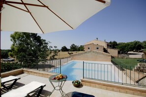 Un espace aménagé au bord de la piscine, avec une table et des chaises, un saladier rempli de fruits et, en arrière-plan, la vue d’un bâtiment.