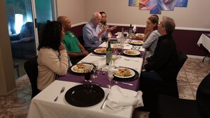 A group of people dining at a table with a purple tablecloth, surrounded by a modern abstract painting. - Richards Travel Lodge (Jamestown)
