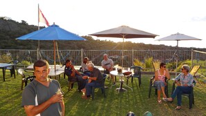 A group of people seated at an outdoor table with umbrellas, surrounded by chairs and a railing. - Richards Travel Lodge (Jamestown)