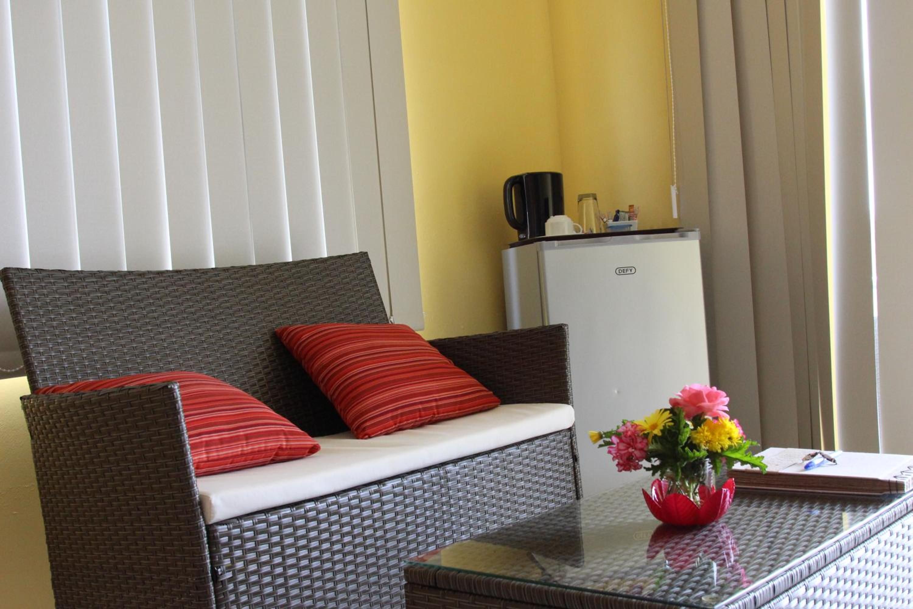 A room with a wicker sofa, a small table with a vase of flowers, and a white cabinet.
