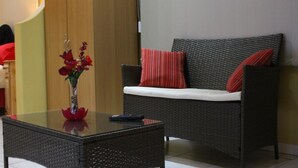 A wicker sofa with red and white cushions, a glass coffee table with a vase of red flowers, and a remote control on the table. - Richards Travel Lodge (Jamestown)